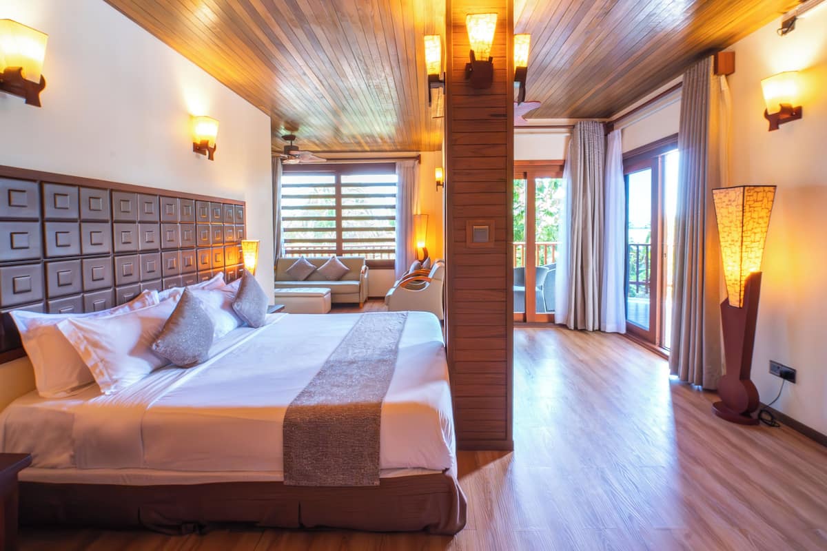 A spacious hotel room with a large bed, wooden ceiling, and multiple wall sconces.