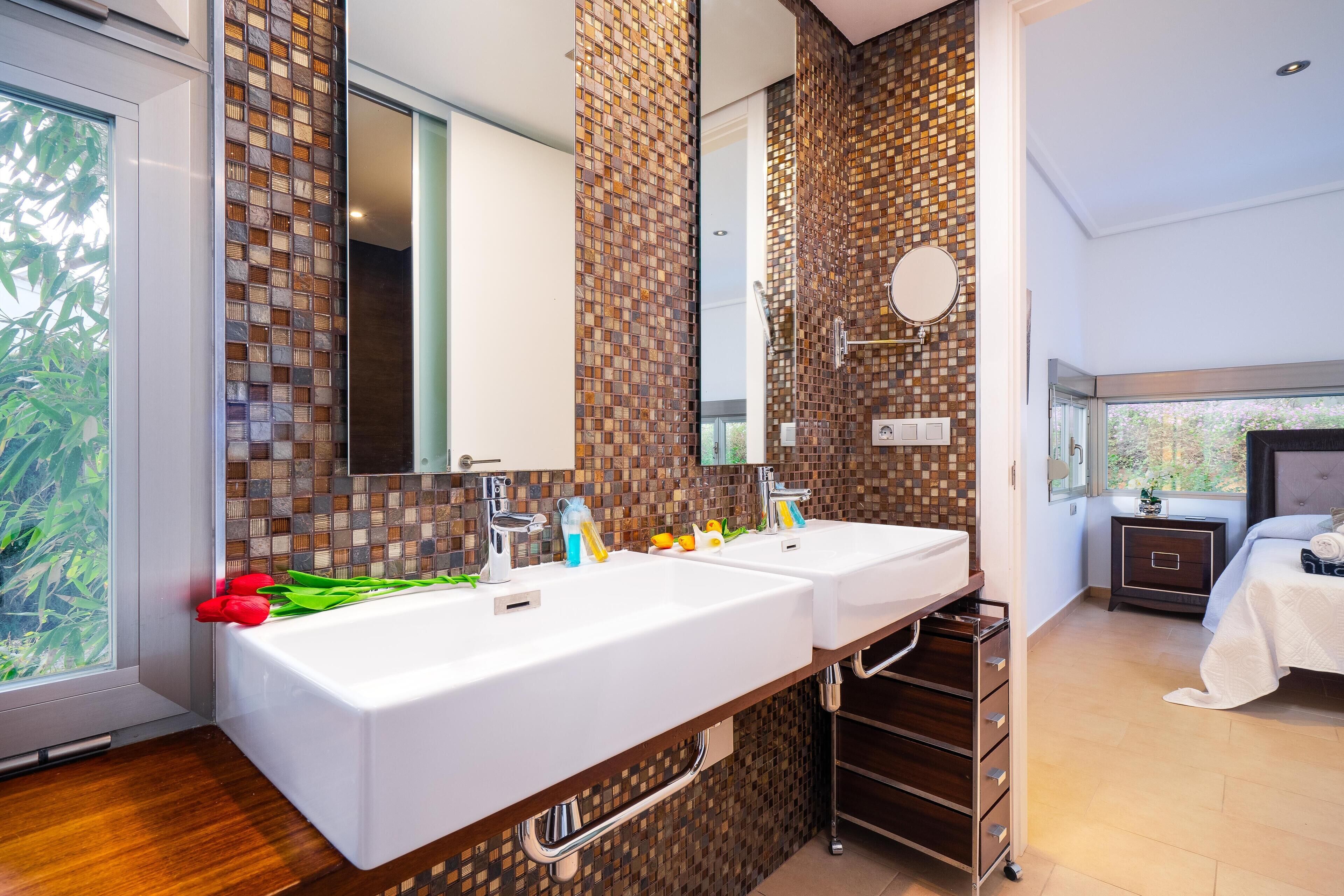 A modern bathroom with two sinks, a large mirror, and a view of greenery outside.