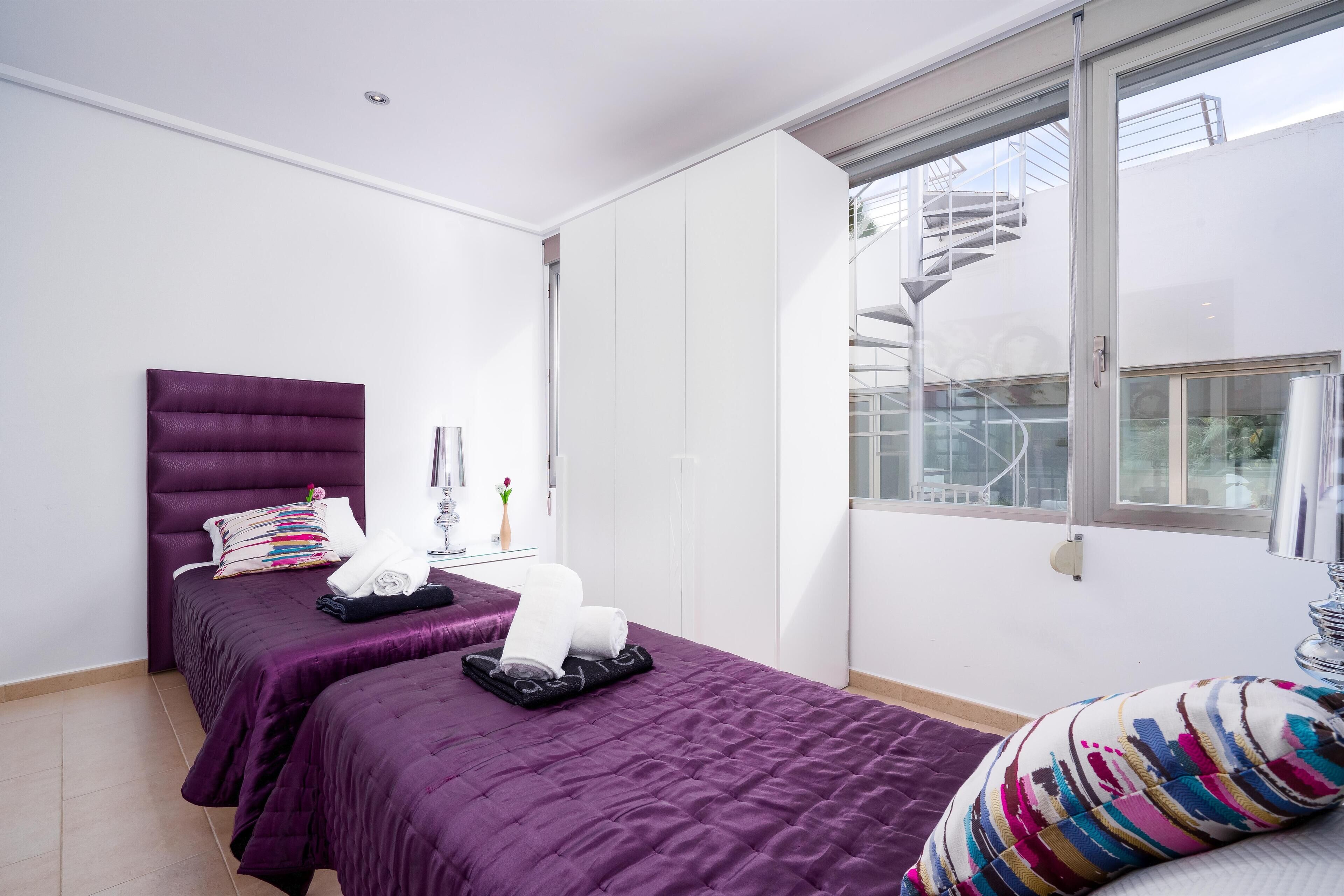 Habitació d'hotel moderna amb dos llits, un gran finestral i vista a un edifici amb una escala espirall.