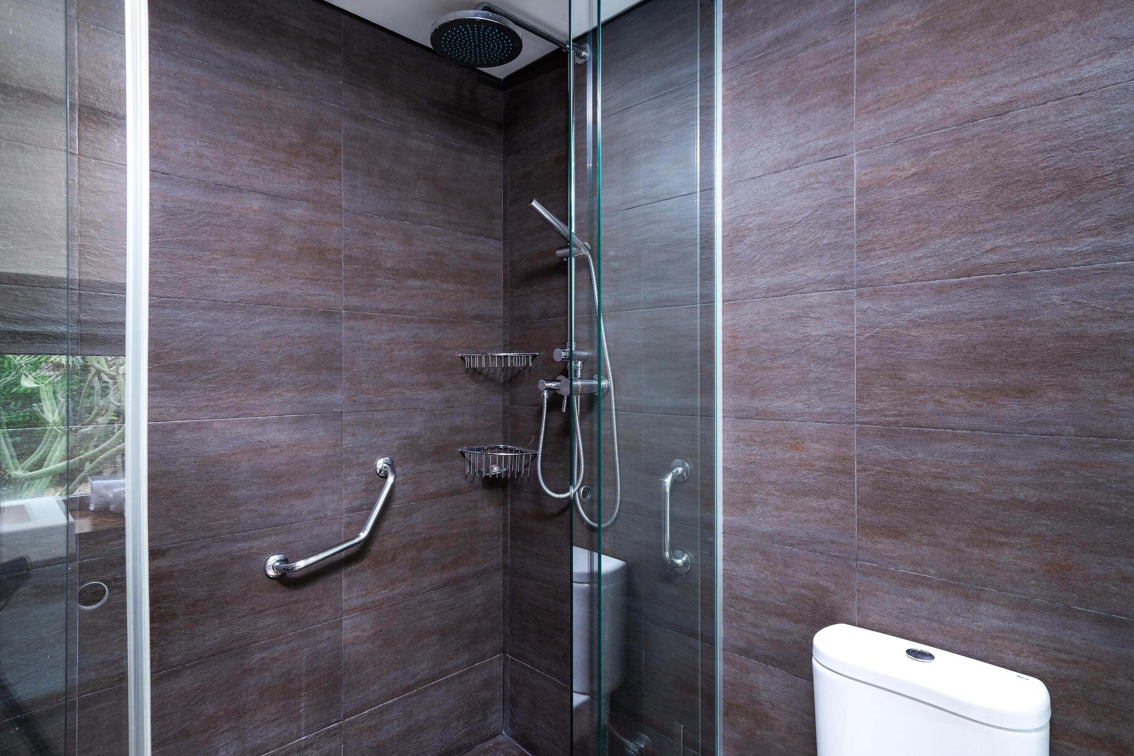 A modern bathroom with a glass shower enclosure, a white toilet, and a handrail.