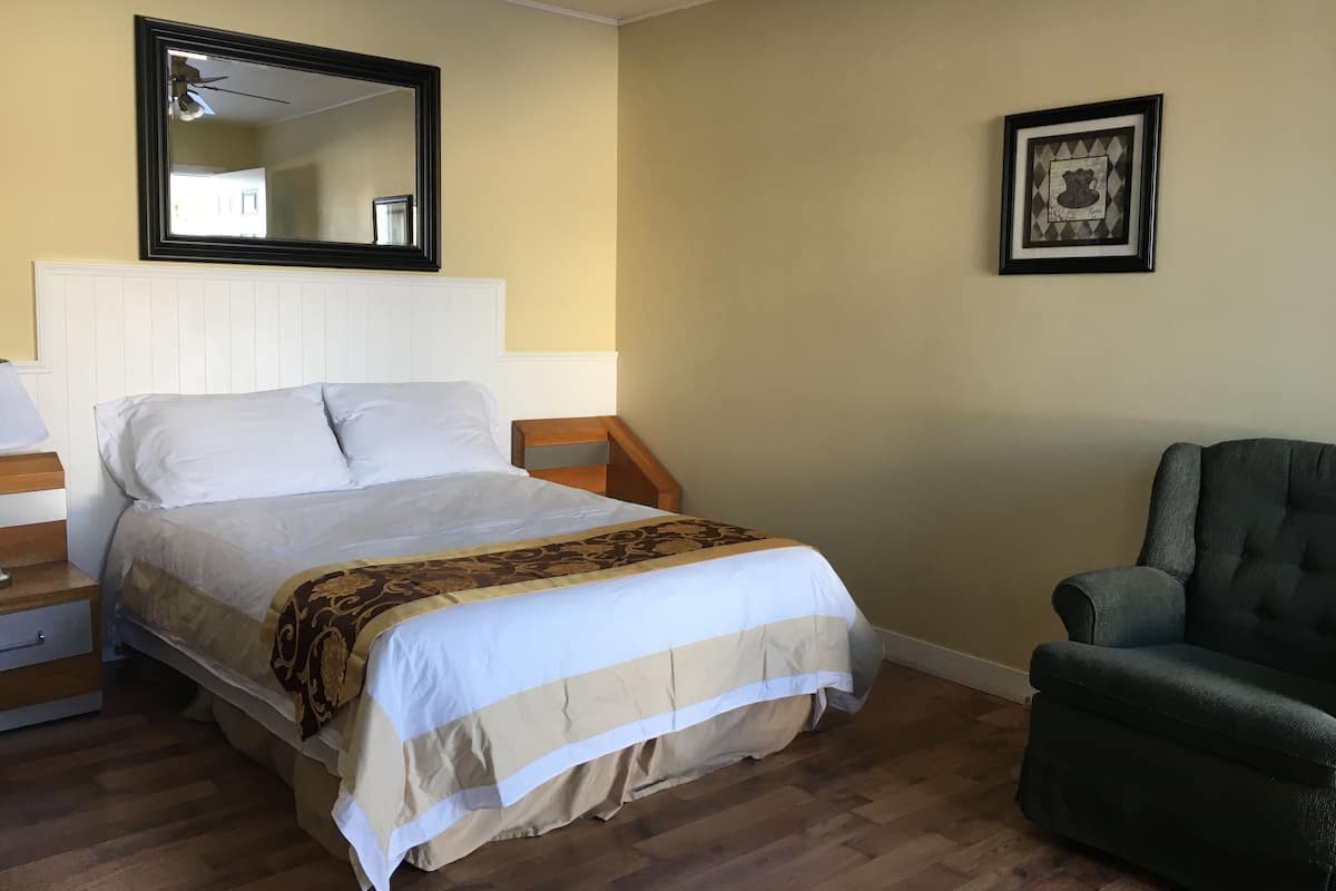 A bedroom with a bed, nightstands, a chair, a mirror, and a framed picture on the wall.