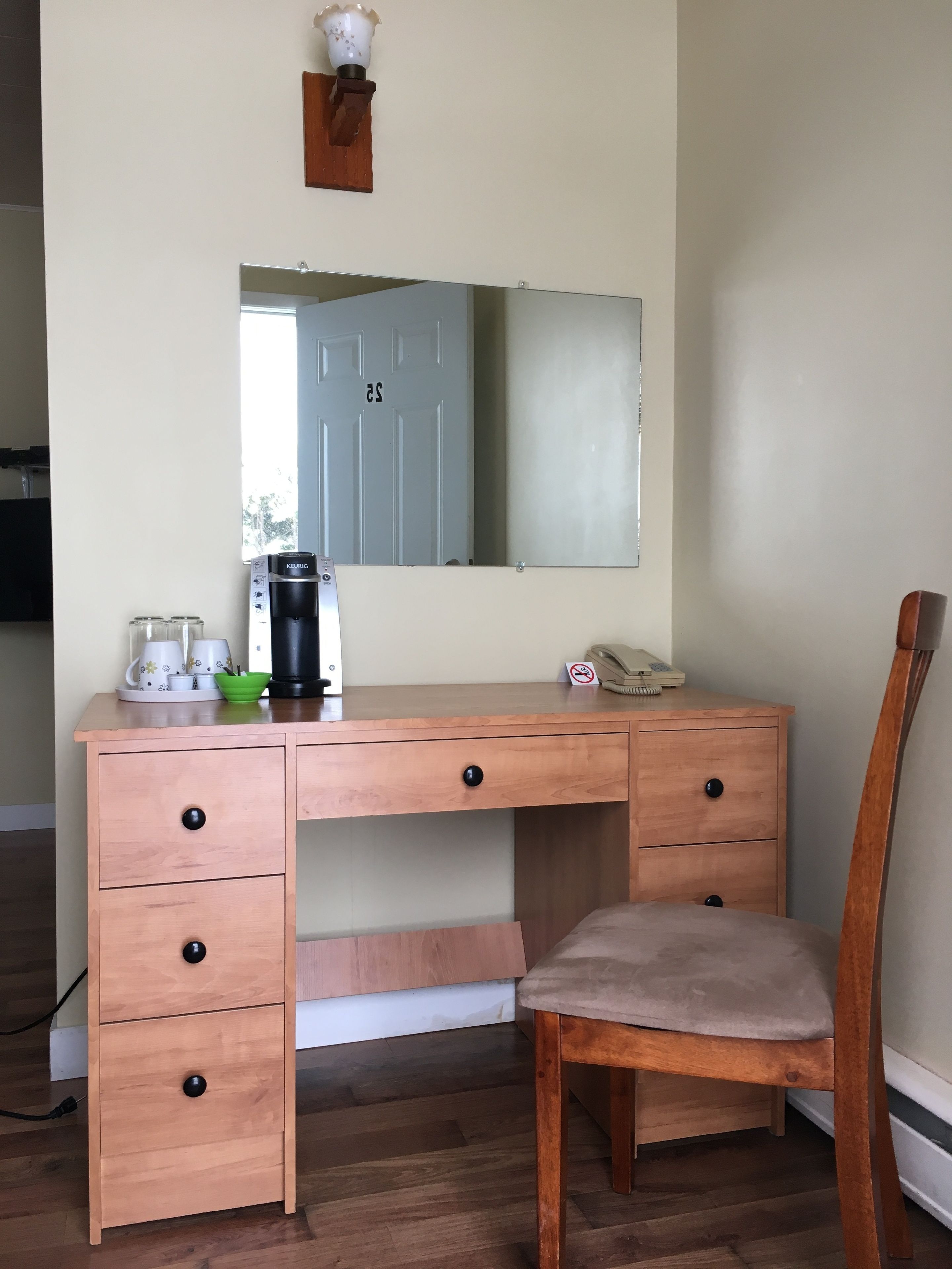 Ein Holztisch mit Spiegel, einer Kaffeemaschine und einem Stuhl.