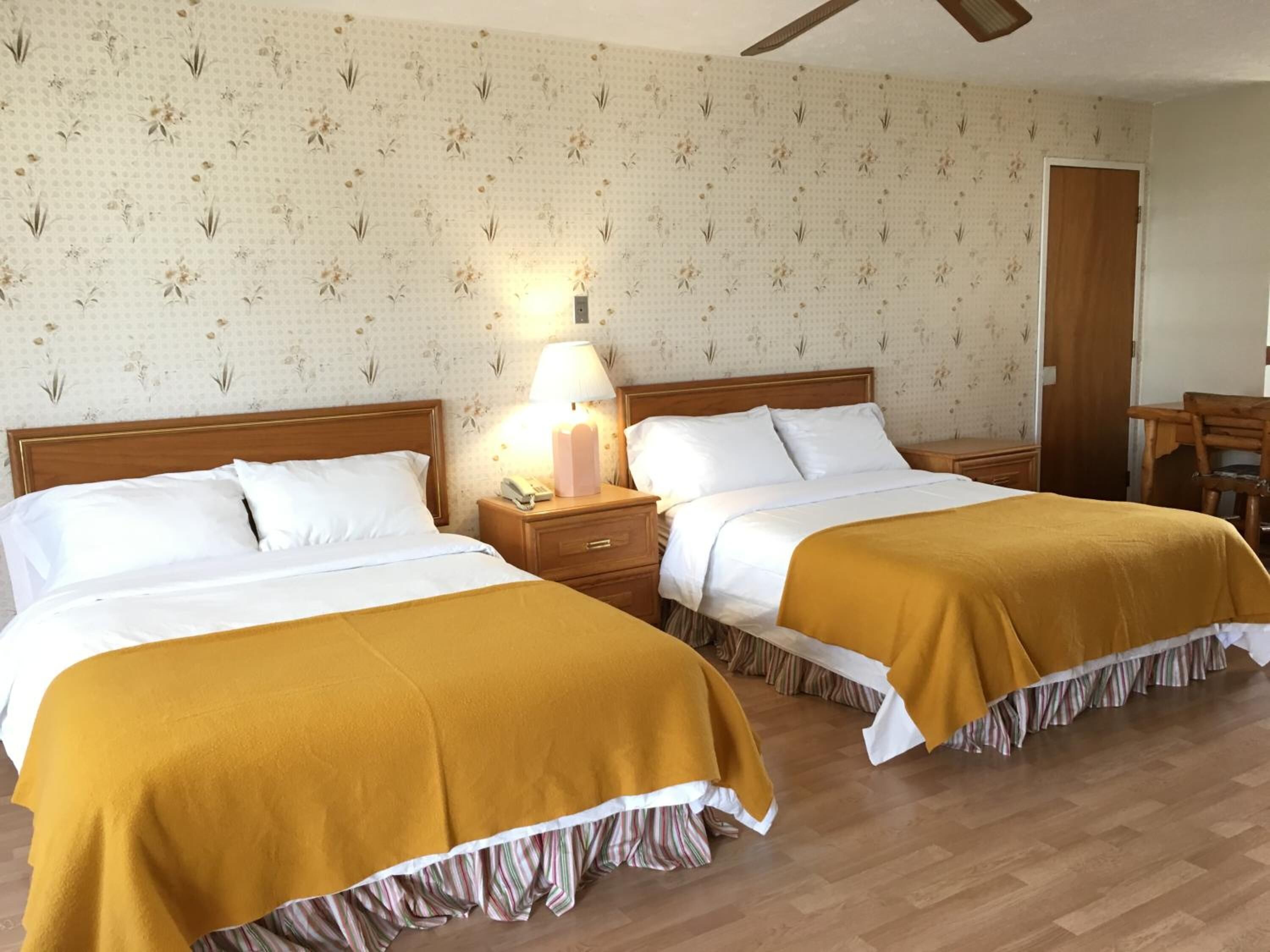 A hotel room with two beds, wooden headboards, a nightstand with a lamp, a wooden chair, and a wooden door.