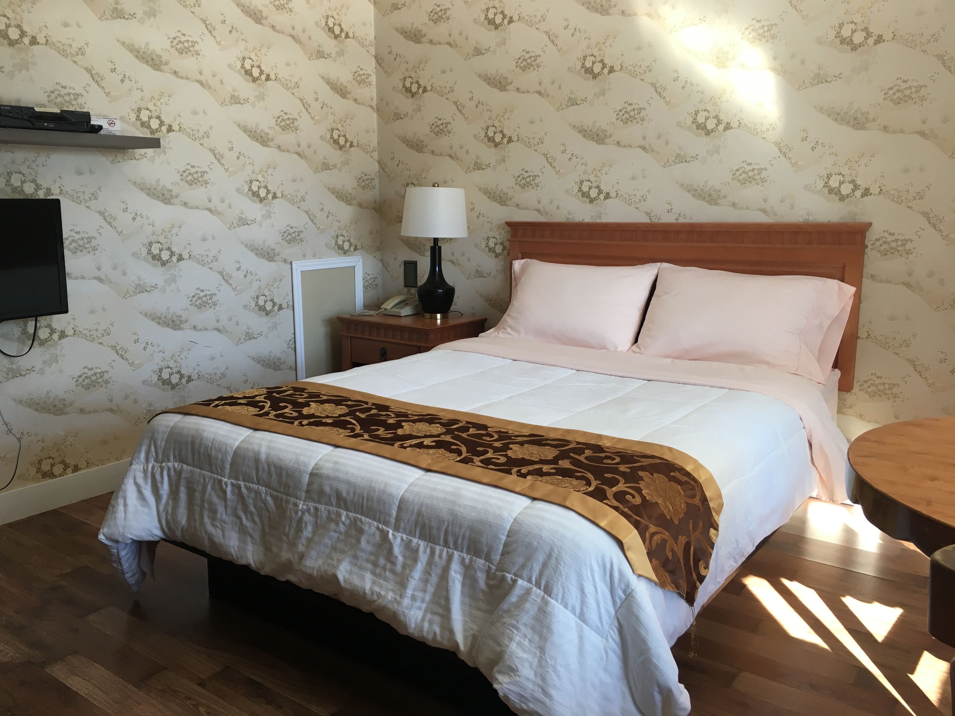 A neatly made bed with a patterned bedspread, a bedside lamp, and a wooden nightstand with a telephone.