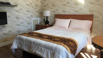 A neatly made bed with a patterned bedspread, a bedside lamp, and a wooden nightstand with a telephone.