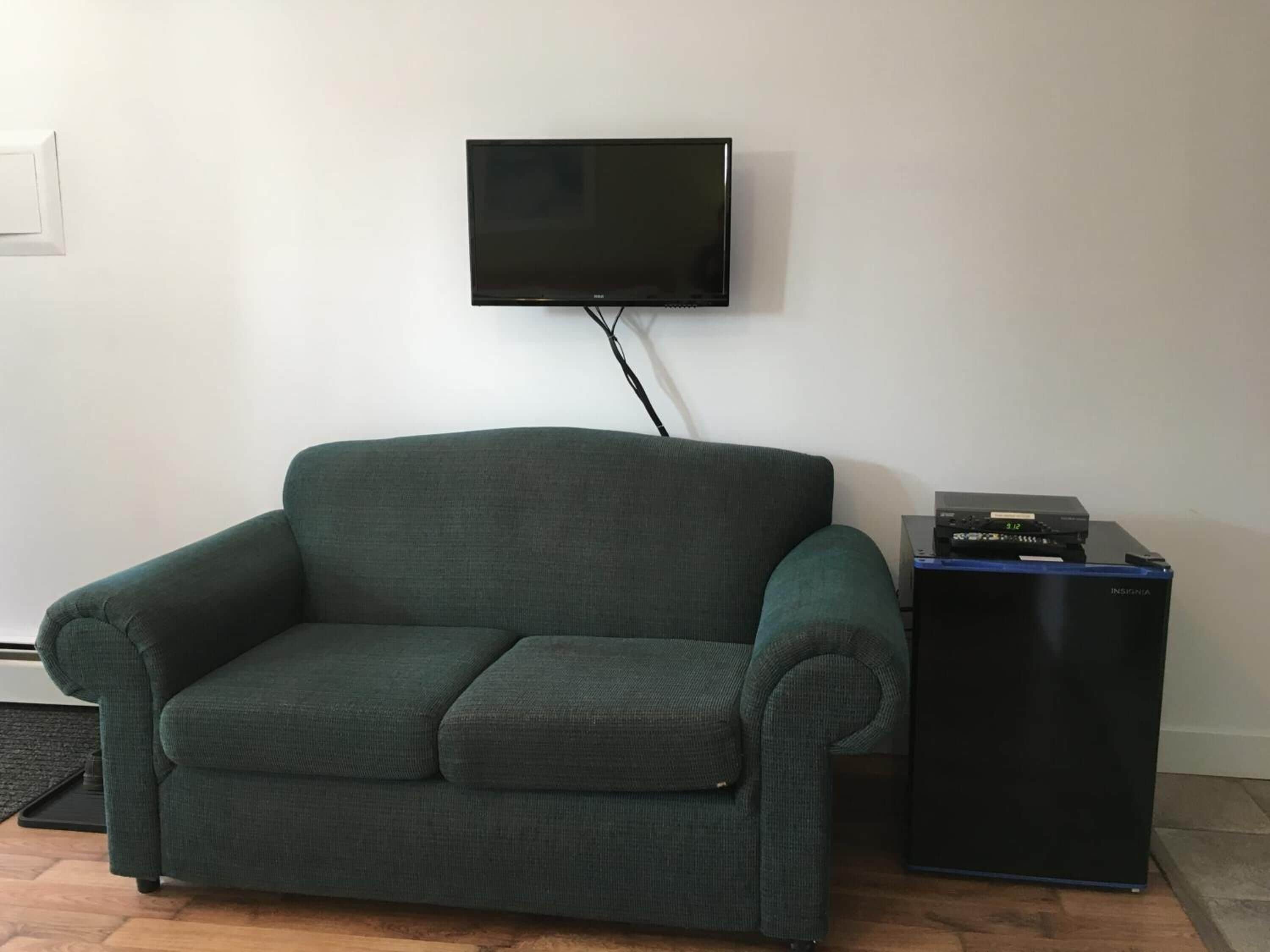 Un sofá verde oscuro con un reposapiés a juego, un televisor de pantalla plana montado en la pared y un mueble de entretenimiento negro con dispositivos electrónicos.