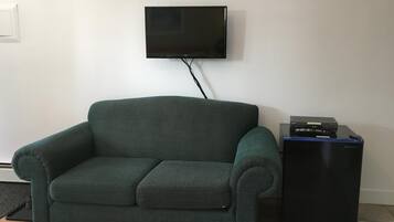 Un sofá verde oscuro con un reposapiés a juego, un televisor de pantalla plana montado en la pared y un mueble de entretenimiento negro con dispositivos electrónicos.