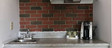 Una cucina compatta con mobili in legno, zoccolo in mattoni, microonde integrato e macchina da caffè.