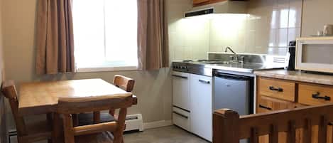 Een kleine keuken met een eettafel, houten stoelen, een fornuis, een spoelbak en een magnetron.
