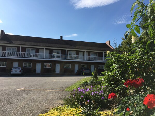 A two-story building with a balcony, parked cars, and a garden with flowers. - Motel Le Sabre (Sherbrooke)