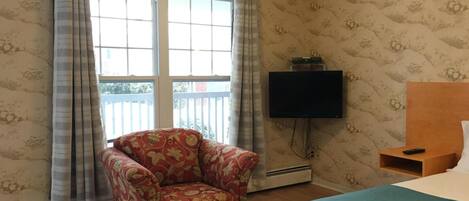 A room with a bed, a chair, a television, and a window with curtains.