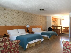 A hotel room with two beds, a wooden headboard, a patterned wallpaper, a wooden floor, a desk, and a chair. - Motel Le Sabre (Sherbrooke)