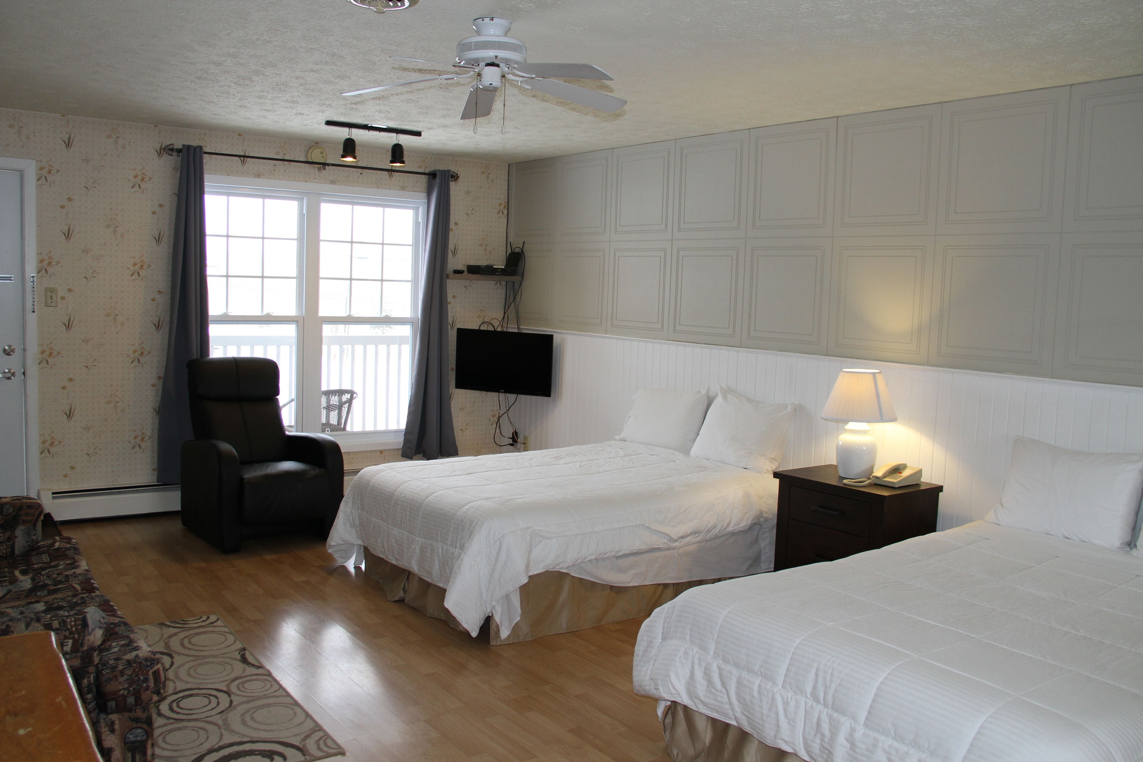 Habitación de hotel con dos camas, una silla, un televisor y un ventilador de techo.