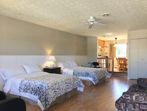 A hotel room with two beds, a ceiling fan, a dining area with a table and chairs, and a door. - Motel Le Sabre (Sherbrooke)