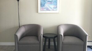 Deux fauteuils gris, une petite table ronde placée entre eux, un lampadaire et un tableau encadré accroché au mur.