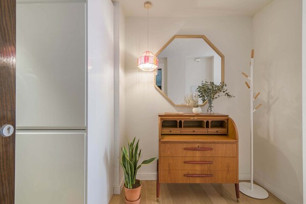 A hallway with a wooden dresser, a potted plant, and a mirror on the wall.