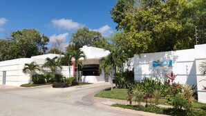 A modern building with a white facade, a gated entrance, and a landscaped area with various plants.