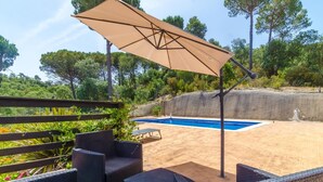 Un área de piscina al aire libre con un deck de arena, rodeada de exuberante follaje y árboles altos.