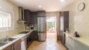 Una cocina moderna con electrodomésticos de acero inoxidable, microondas y refrigerador. Hay una ventana a la izquierda y un reloj en la pared.