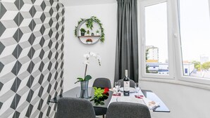 A dining area with a table set for two, a potted orchid, a wine bottle, and a wall-mounted plant shelf. - HAppy House (Cascais)