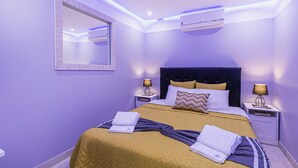 A modern bedroom with a large bed, two bedside tables with lamps, a wall-mounted air conditioner, and a mirror. - HAppy House (Cascais)