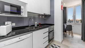A modern kitchen with a dishwasher, microwave, and stove. There is a dining area with a table and chairs. - HAppy House (Cascais)
