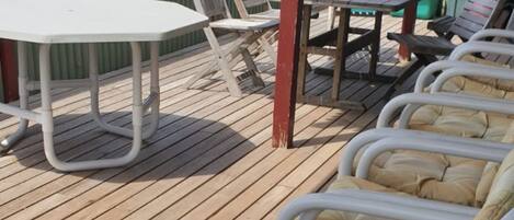 A wooden deck with a table and chairs, and a row of lounge chairs with cushions.