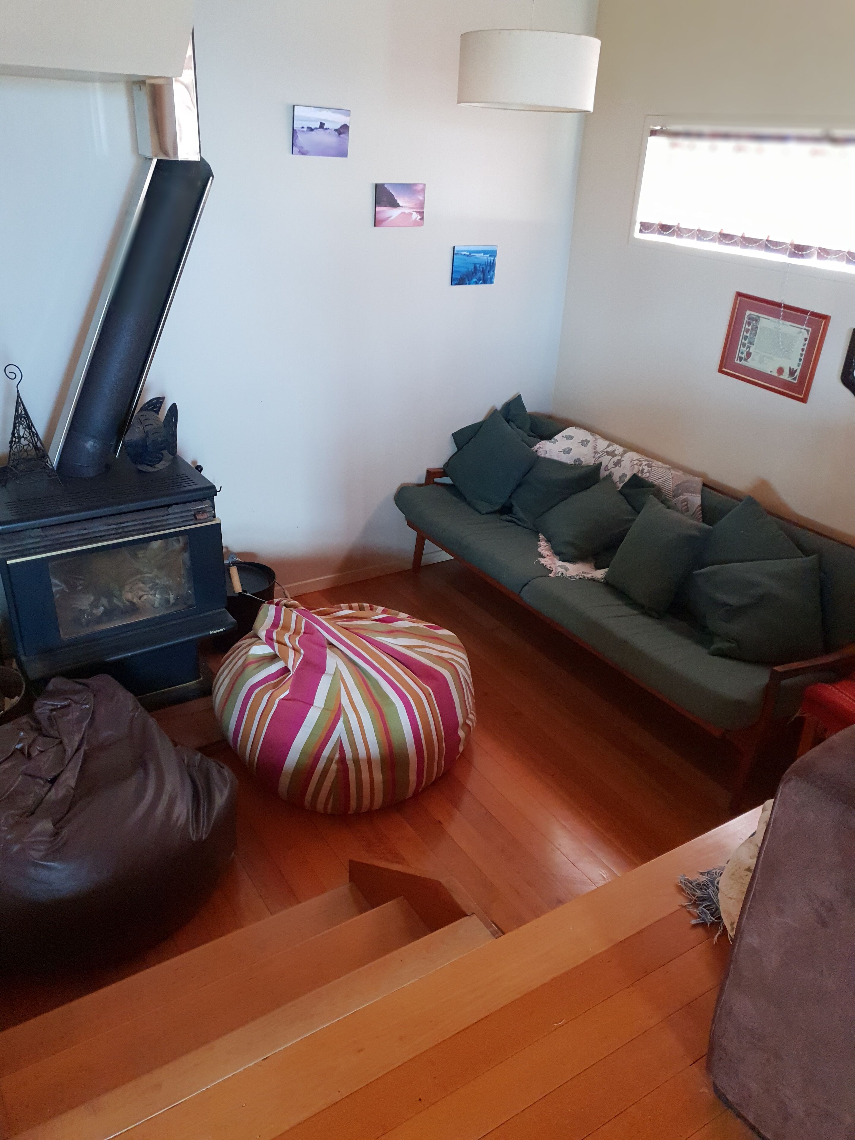 A cozy living room with a sofa, a colorful bean bag, a wooden floor, a fireplace, and wall art.