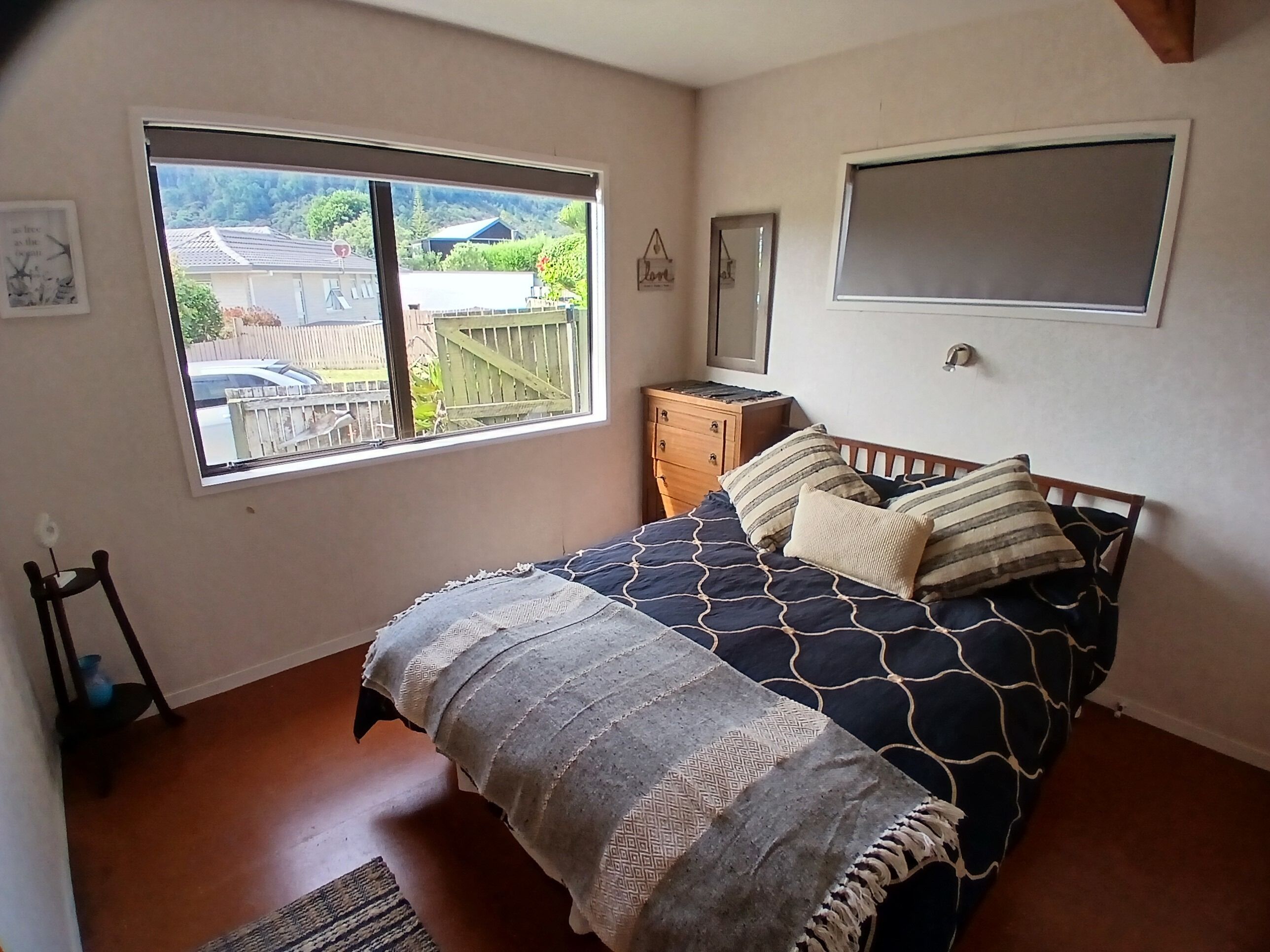 A bedroom with a bed, a dresser, a window with a view of a house and trees, and a wall-mounted shelf.