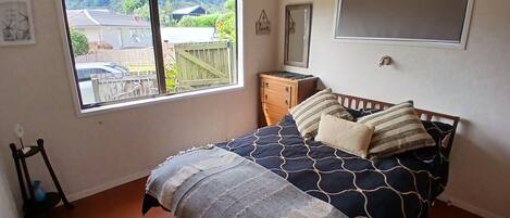 A bedroom with a bed, a dresser, a window with a view of a house and trees, and a wall-mounted shelf.