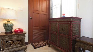 Um quarto com porta de madeira, um armário decorativo, uma pequena mesa com abajur e um vaso vermelho.