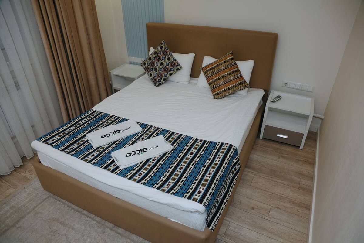 Une chambre d’hôtel avec un lit, une table de chevet avec un téléphone et une fenêtre avec des rideaux.