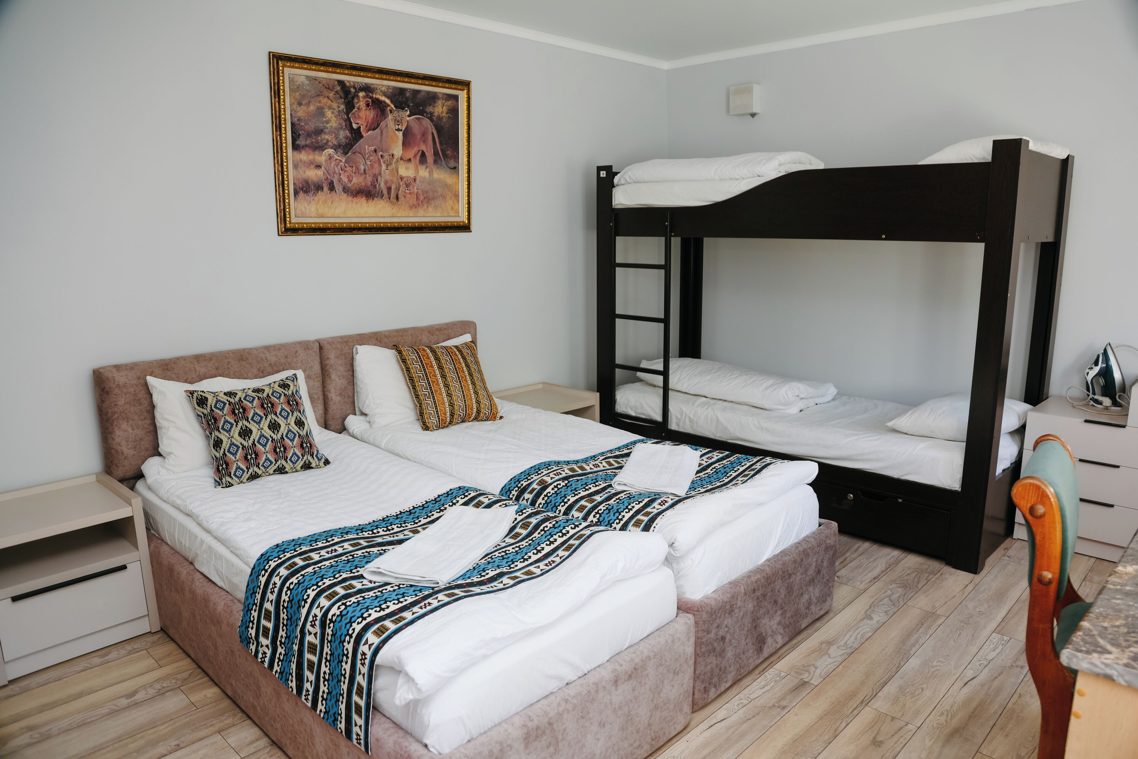 A bedroom with a bunk bed, a sofa bed, a bedside table, a chair, and a painting on the wall.