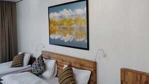 A hotel room with two beds, a wooden headboard, a painting of a mountain landscape, and a view of a lake. - Apple Hostel (Bishkek)