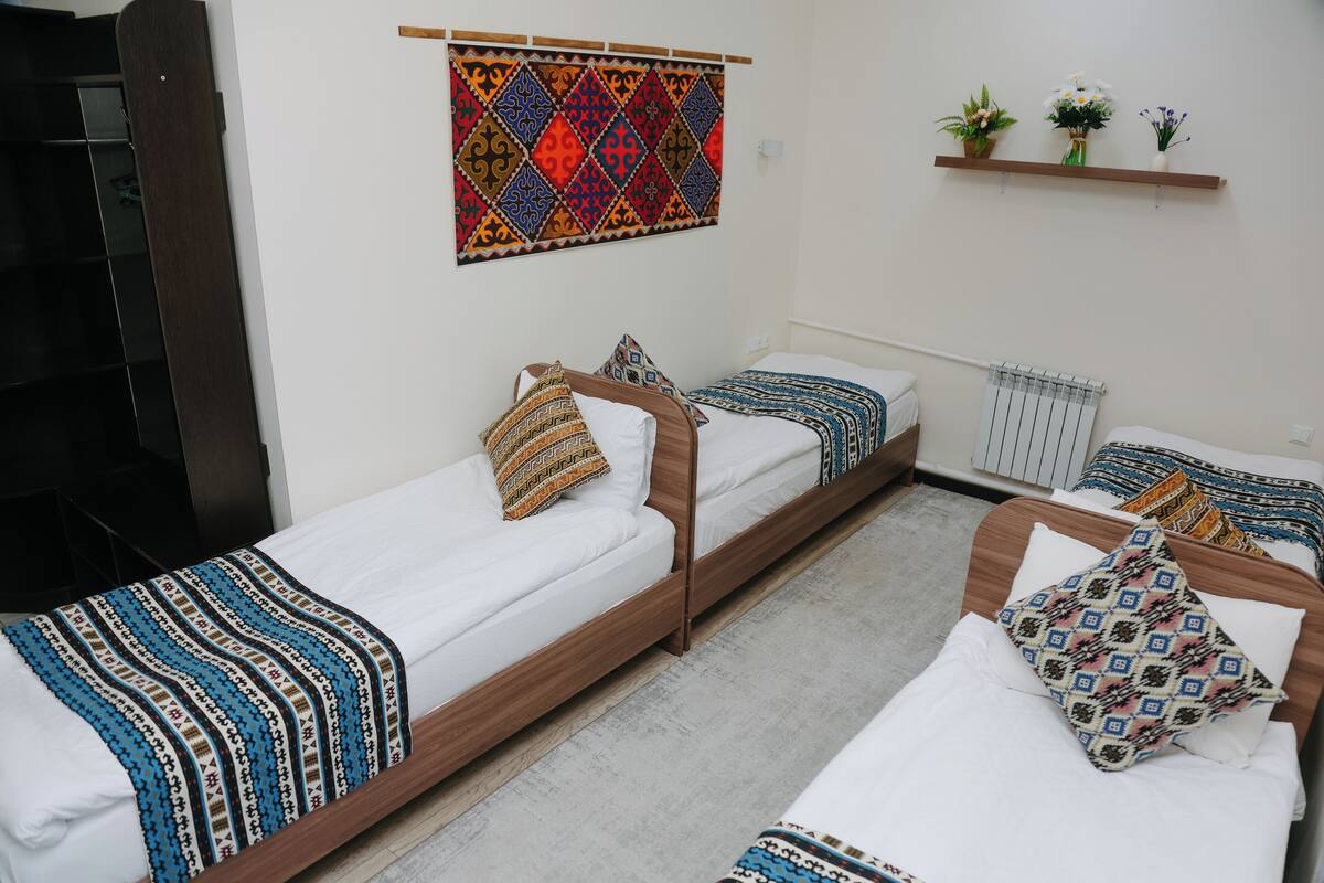 Une chambre avec deux lits simples, une tête de lit en bois, une décoration murale colorée et une étagère avec des plantes.