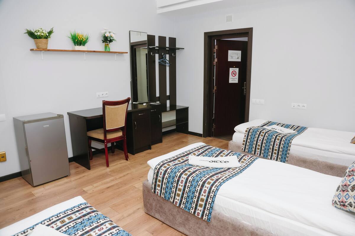 Une chambre d’hôtel équipée d’un bureau, d’une chaise, de deux lits, d’un miroir, d’un petit réfrigérateur et d’une porte avec une pancarte.