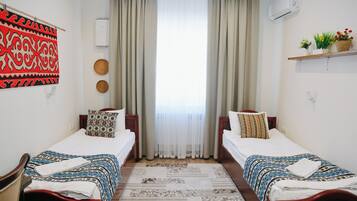 Una habitación de hotel con dos camas individuales, un ventanal con cortinas, un aire acondicionado de pared y un estante con adornos.
