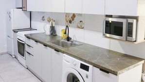 A modern kitchen with white cabinets, a built-in microwave, a washing machine, and a coffee-themed backsplash. - Apple Hostel (Bishkek)
