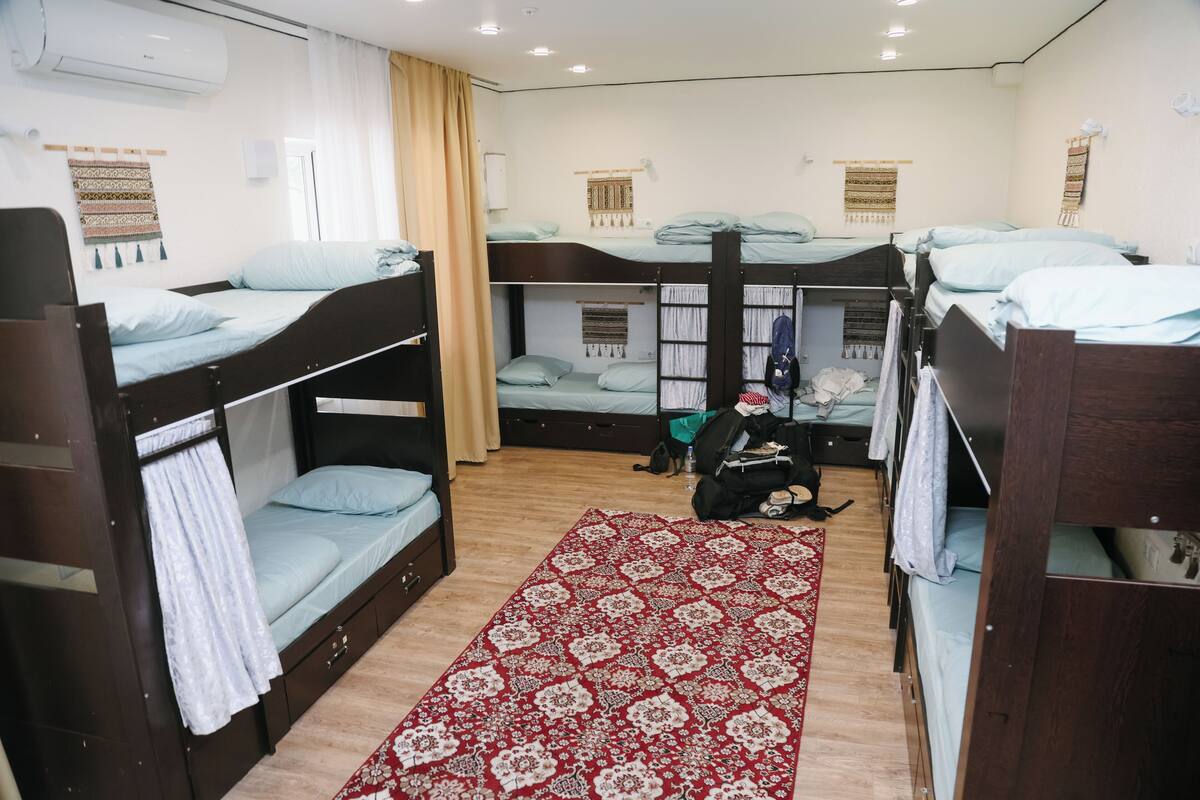 Une chambre de dortoir avec des lits superposés, un tapis à motifs et un petit coin salon.