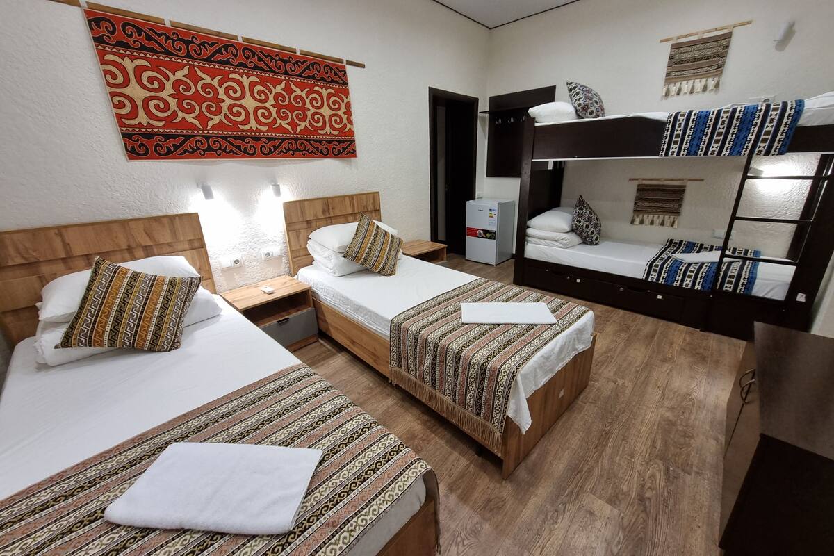 Une chambre d’hôtel avec deux lits simples, un lit superposé, un petit bureau et un téléviseur fixé au mur.