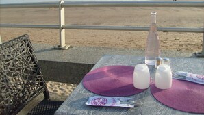 Een gedekte tafel met een fles, glazen en bestek, uitkijkend over de zee.