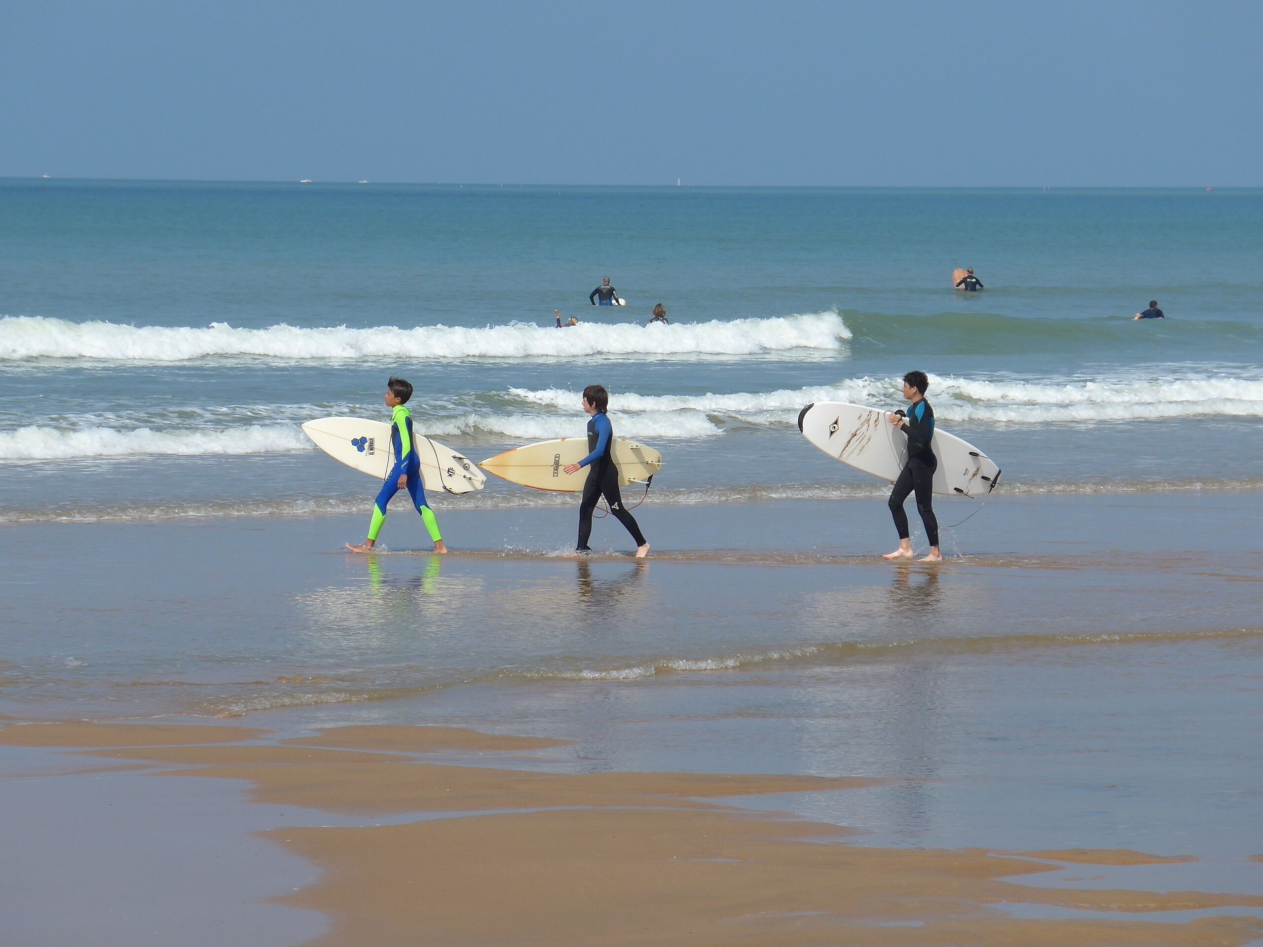 A beach with surfers walking towards the water, carrying surfboards.