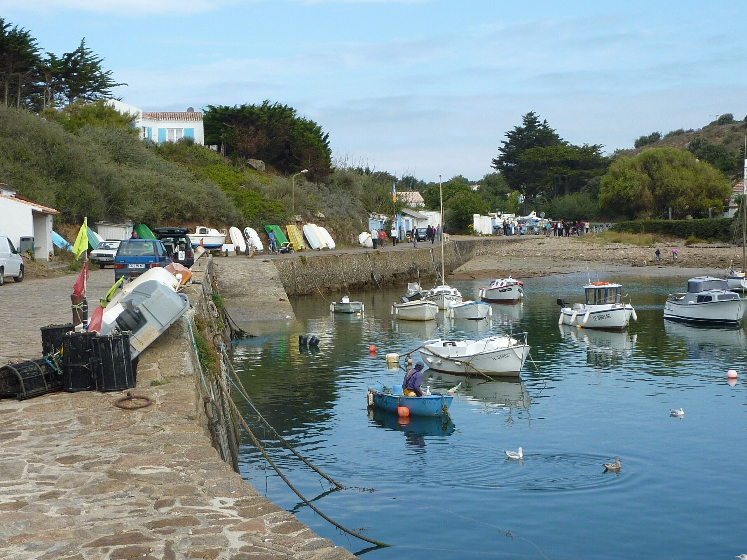 A harbor with boats docked, a stone wall, and a few people walking by.