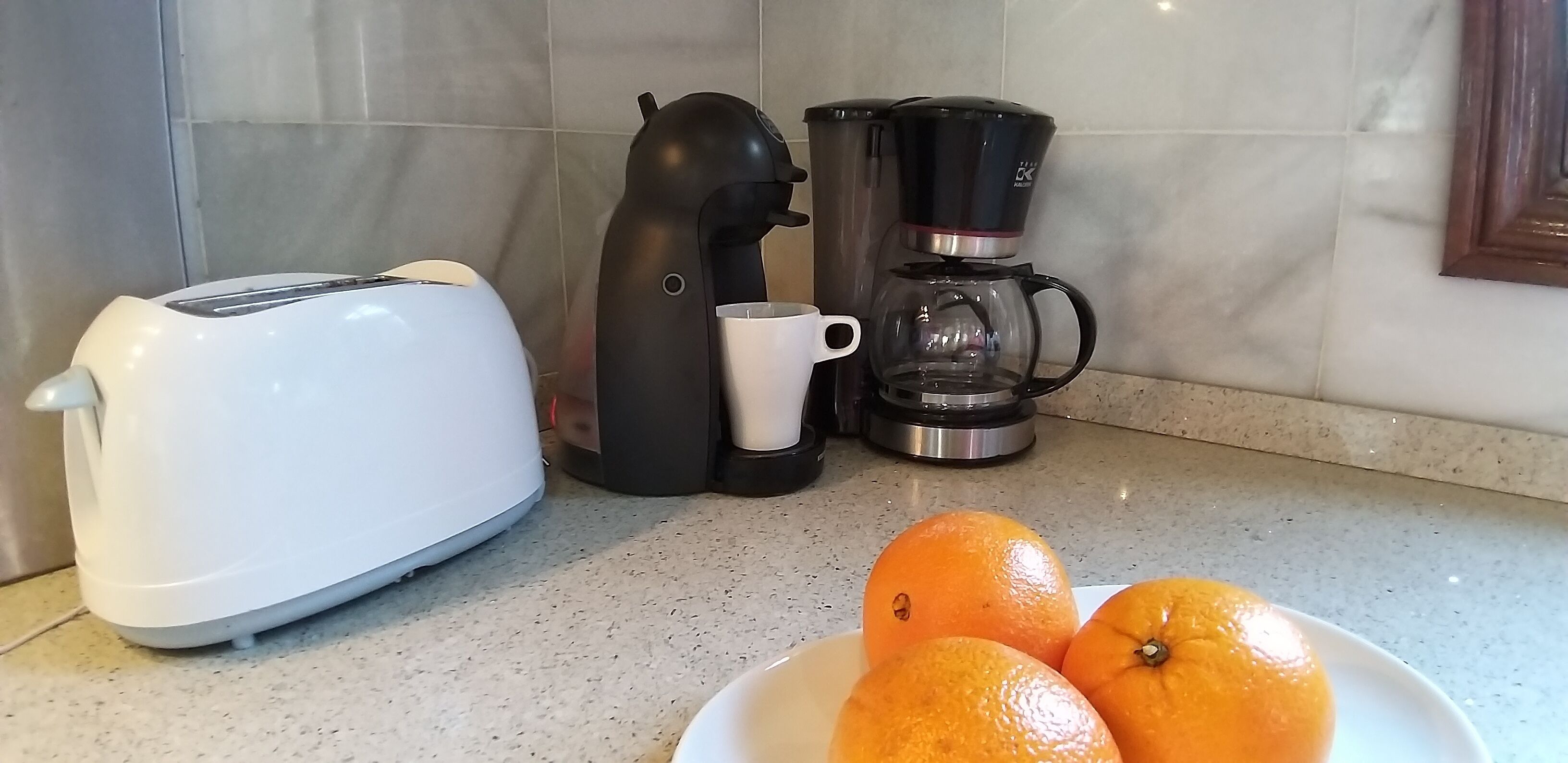 Een keukentafel met een broodrooster, een koffiezetapparaat en een bord sinaasappels.