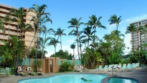 A pool area with lounge chairs and palm trees, surrounded by hotel buildings.