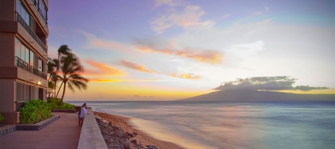 A beachfront hotel with a view of the ocean and a sunset.