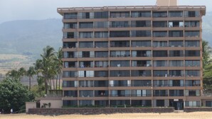 A multi-story hotel with a flat roof, located near a beach.