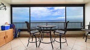 A balcony with a table and chairs, a view of the sea, and a ceiling light fixture.