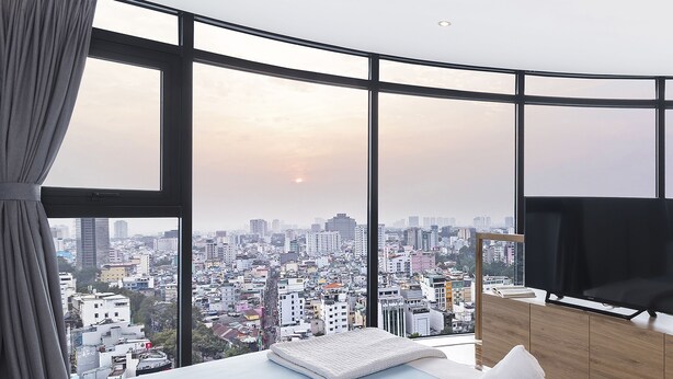 A bedroom with a city view, a bed, a TV, and a wooden dresser.