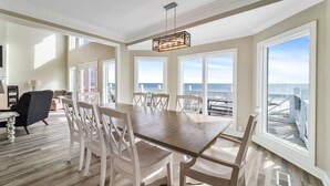 A spacious dining area with a large wooden table and white chairs, large windows with ocean views, and a modern pendant light. - Luxury gulf front home with huge windows facing the Gulf. Large open decks (Gulf Shores)